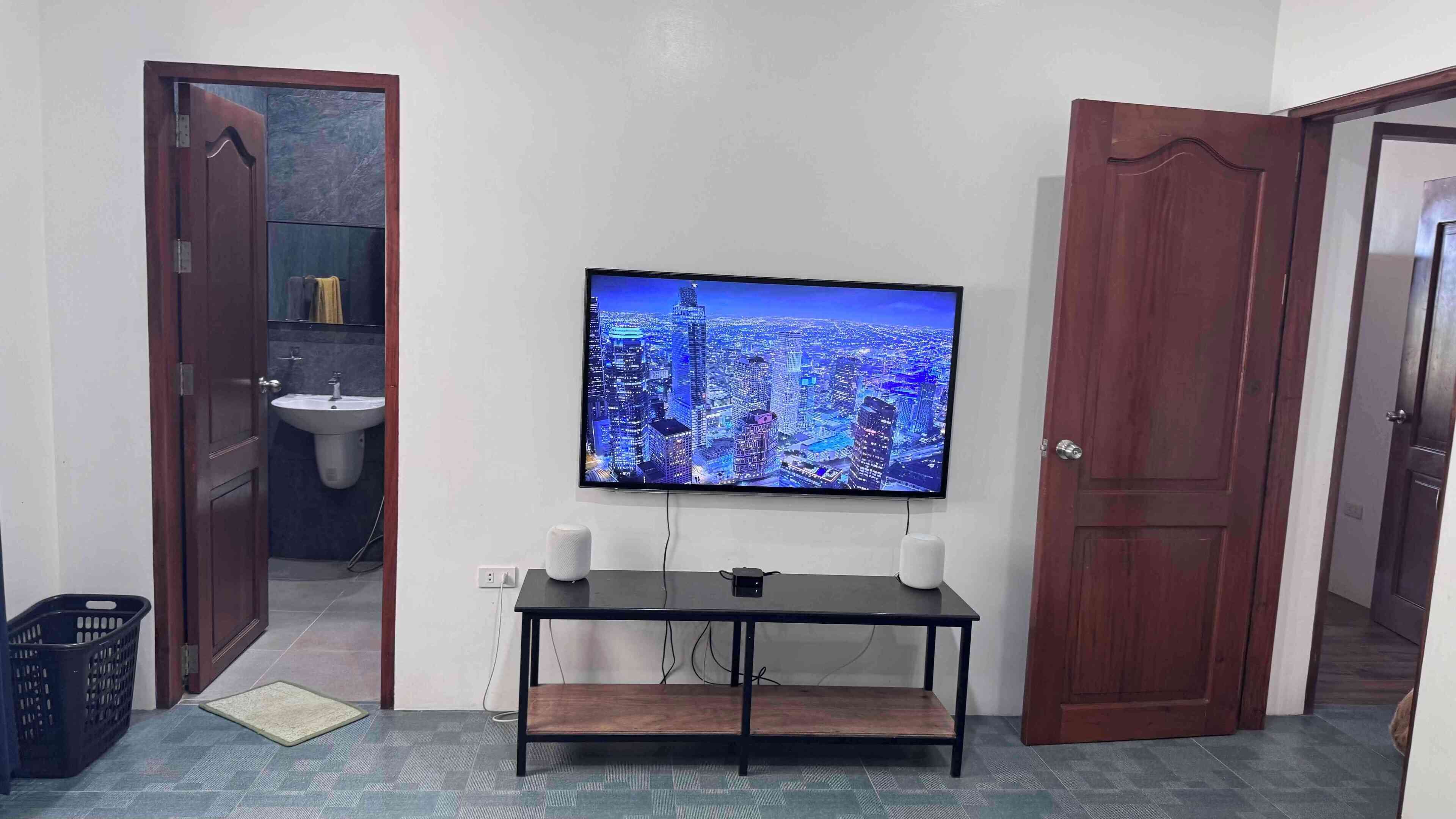 A room with a TV mounted on the wall, a small table, and a door leading to a bathroom.