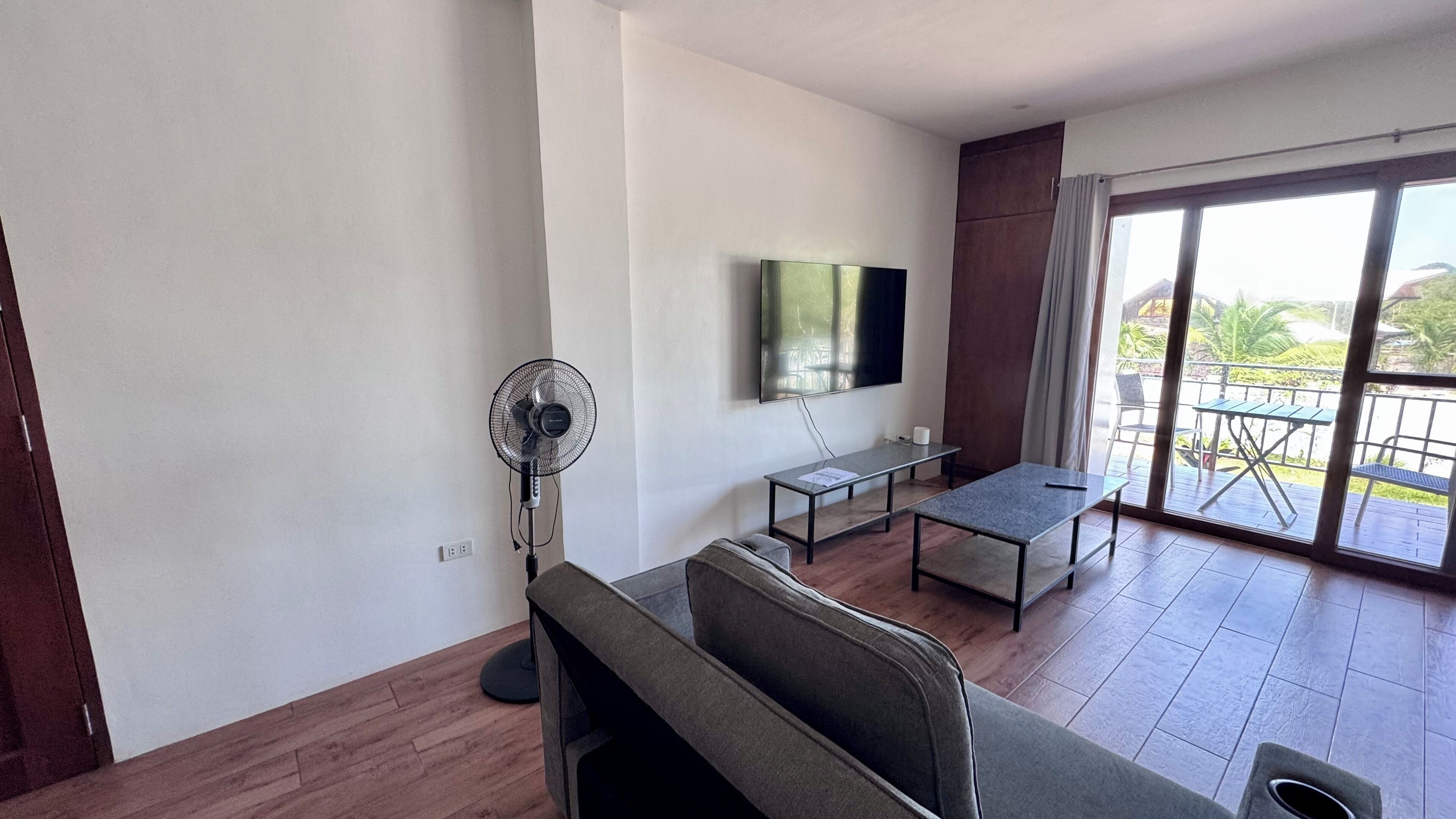 A modern living room with a sofa, a small table, a TV, and a balcony with outdoor furniture.