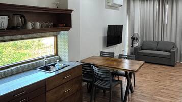 A modern kitchen with wooden cabinets, a dining area with a table and chairs, a grey sofa, and a TV mounted on the wall.