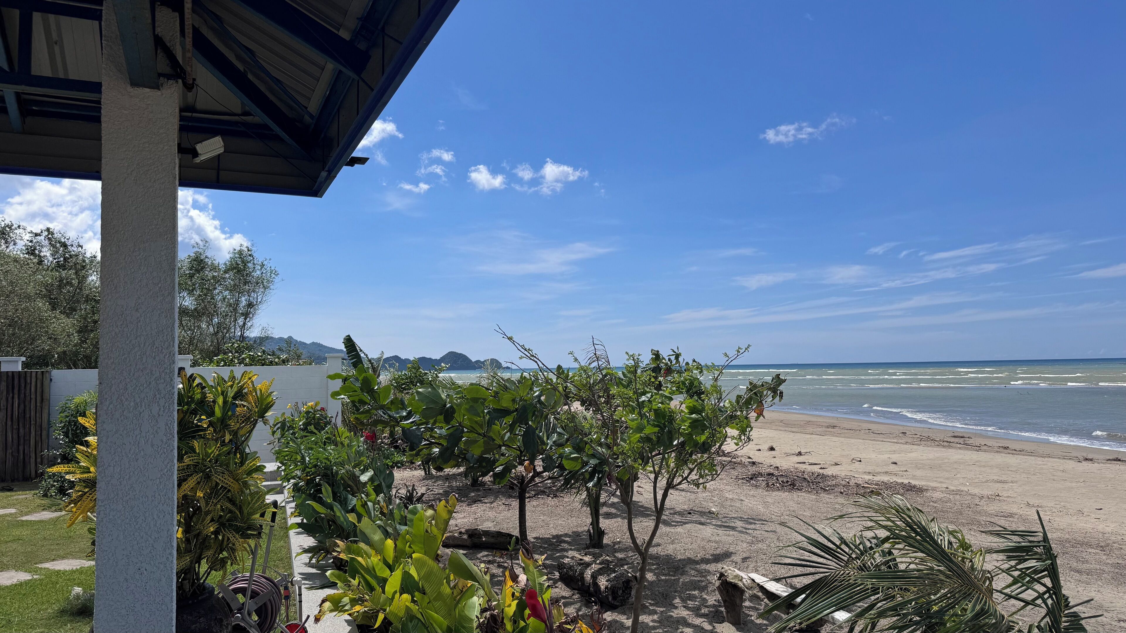 A beach view with a covered area and lush greenery in the foreground.