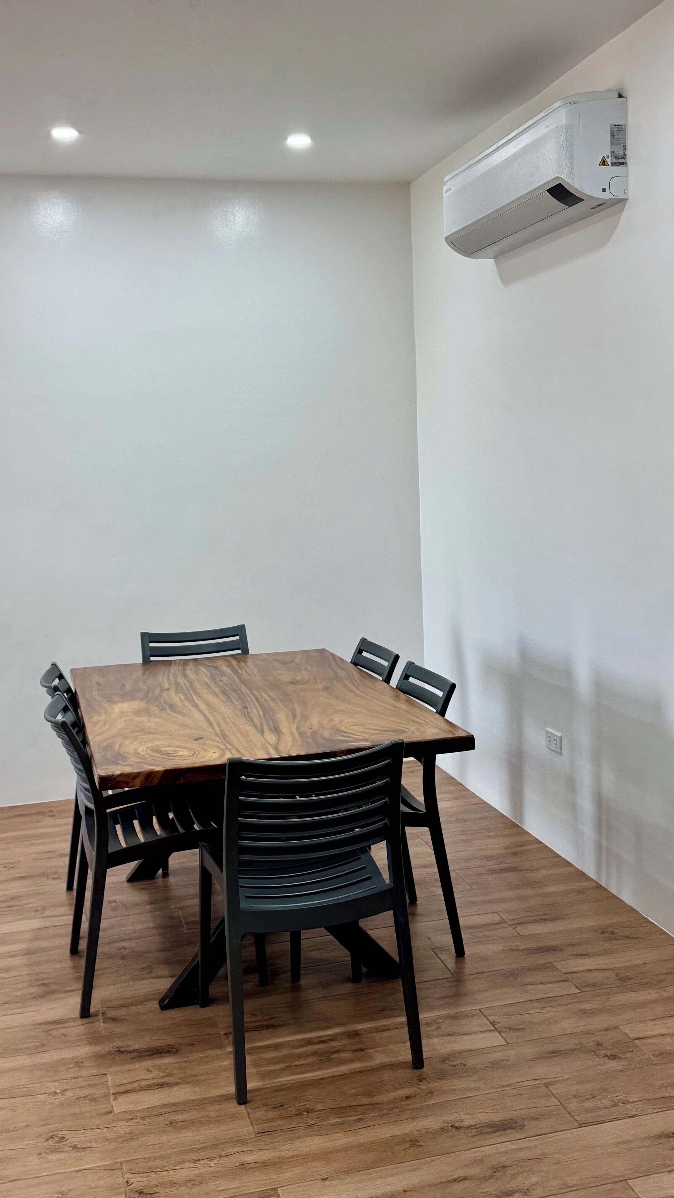 Una sala de conferències amb una taula de fusta i cadires negres, una paret blanca i una unitat de climatització penjada a la paret.