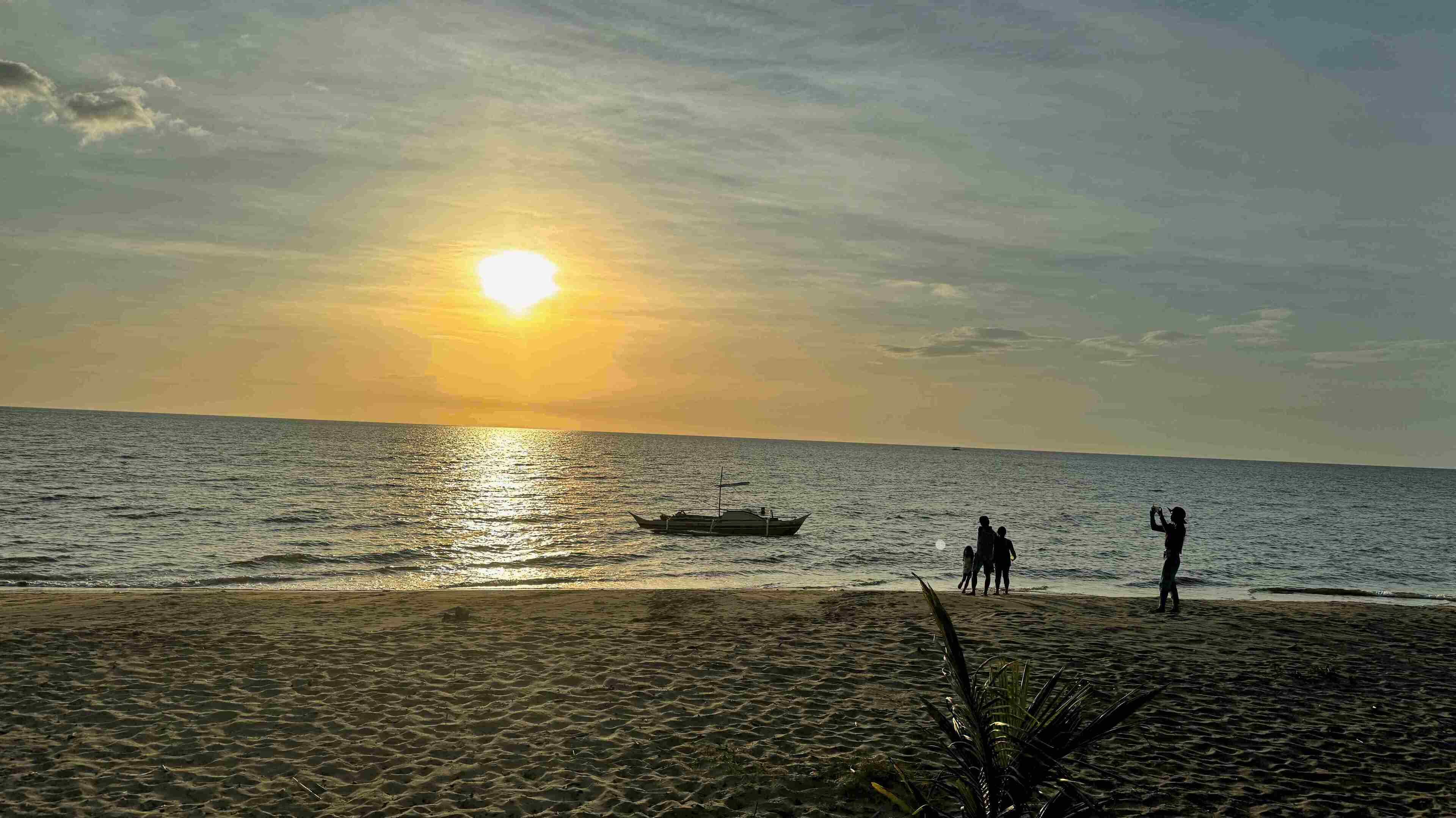 A beach with a boat on the water and people walking along the shore.