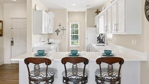 A modern kitchen with white cabinetry, a central island with bar stools, and a large wall clock. - 3BR Condo at Royal Links • Golf Course Views • Near Hwy 76 (Branson)