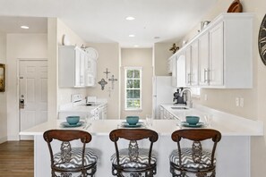 A modern kitchen with white cabinetry, a central island with bar stools, and a large wall clock. - Walk-In 3BR Condo at Royal Links • Golf Course Views • Near Hwy 76 (Branson)