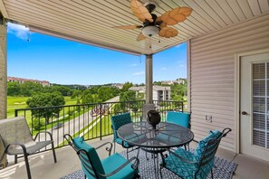 A covered balcony with a table and chairs, a ceiling fan, and a view of a golf course. - Walk-In 3BR Condo at Royal Links • Golf Course Views • Near Hwy 76 (Branson)