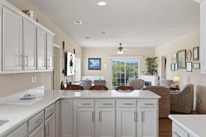 A kitchen with white cabinets, a dining area with chairs, a ceiling fan, and a view through a window. - Walk-In 3BR Condo at Royal Links • Golf Course Views • Near Hwy 76 (Branson)