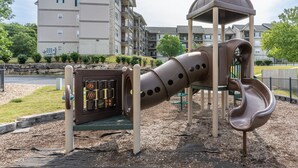 A playground with a slide and climbing structure, surrounded by a landscaped area and residential buildings in the background. - 3BR Condo at Royal Links • Golf Course Views • Near Hwy 76 (Branson)