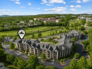 A multi-story hotel with a central courtyard, parking, and surrounding greenery. - Walk-In 3BR Condo at Royal Links • Golf Course Views • Near Hwy 76 (Branson)