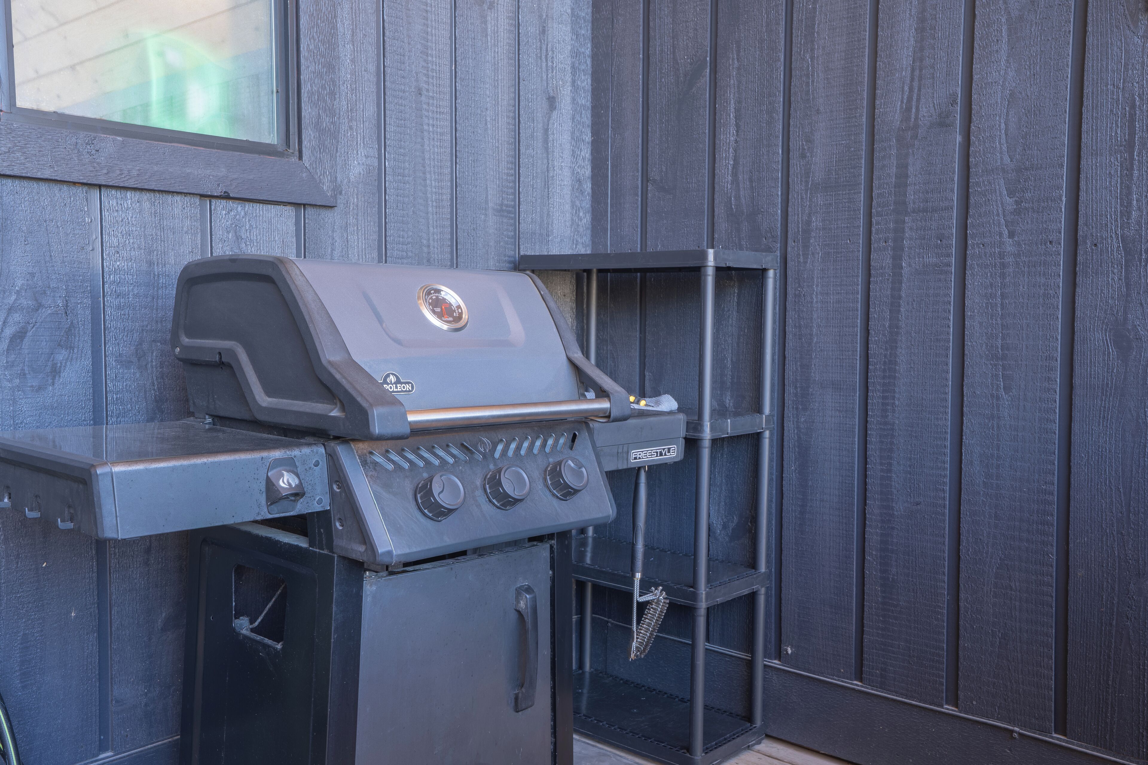 Una parrilla de carbón con panel de control y repisa lateral, frente a una pared de madera.