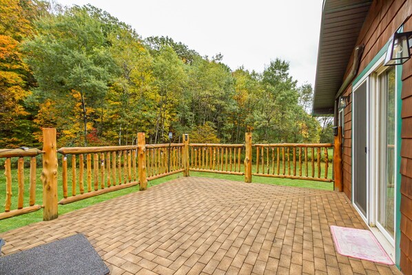 A wooden deck with a brick floor, surrounded by a wooden fence, and a glass door leading to a building. - 3-bedroom rustic cabin on 3.5 acres in Naples with cool AC for relaxing stays (Naples)