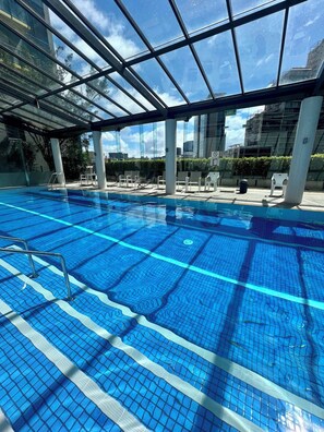 An indoor swimming pool with clear blue water, surrounded by lounge chairs and a glass ceiling. - Welcome to your cosy central apartment in Southbank (Southbank)