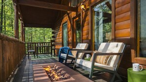 Eine Holzhütte mit verdeckter Veranda, zwei Liegestühlen, einem kleinen Tisch und einem Feuerkorb.