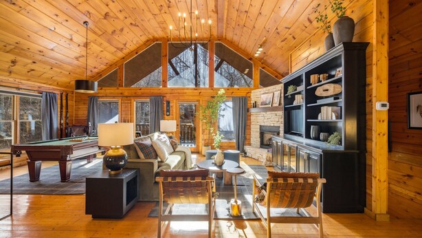 Ein gemütliches Blockhaus-Interieur mit Billardtisch, bequemen Sitzmöglichkeiten, Kamin und einer großen Bücherwand.