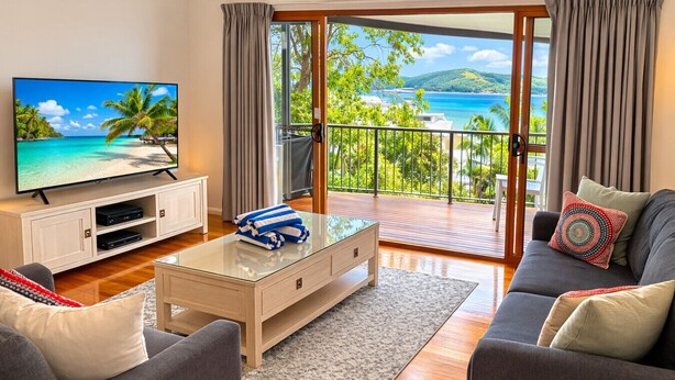 A modern living room with a television, a glass coffee table, and a sofa. - Heliconia 4 & Free Buggy - Hamilton Island (Hamilton Island)