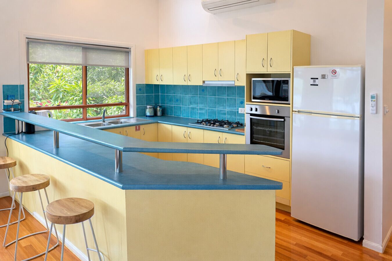 A modern kitchen with a blue countertop, yellow cabinets, a gas stove, a microwave, and a refrigerator.