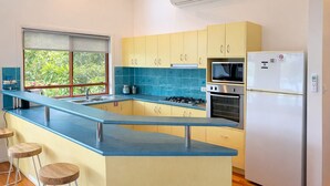 A modern kitchen with a blue countertop, yellow cabinets, a gas stove, a microwave, and a refrigerator. - Heliconia 4 & Free Buggy - Hamilton Island (Hamilton Island)