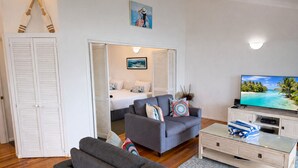 A modern living room with a grey sofa, a television, and a bed with white bedding. - Heliconia 4 & Free Buggy - Hamilton Island (Hamilton Island)