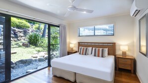 Camera da letto con un letto grande, una ventola a soffitto, una finestra con persiane e vista su un giardino tramite porte in vetro.