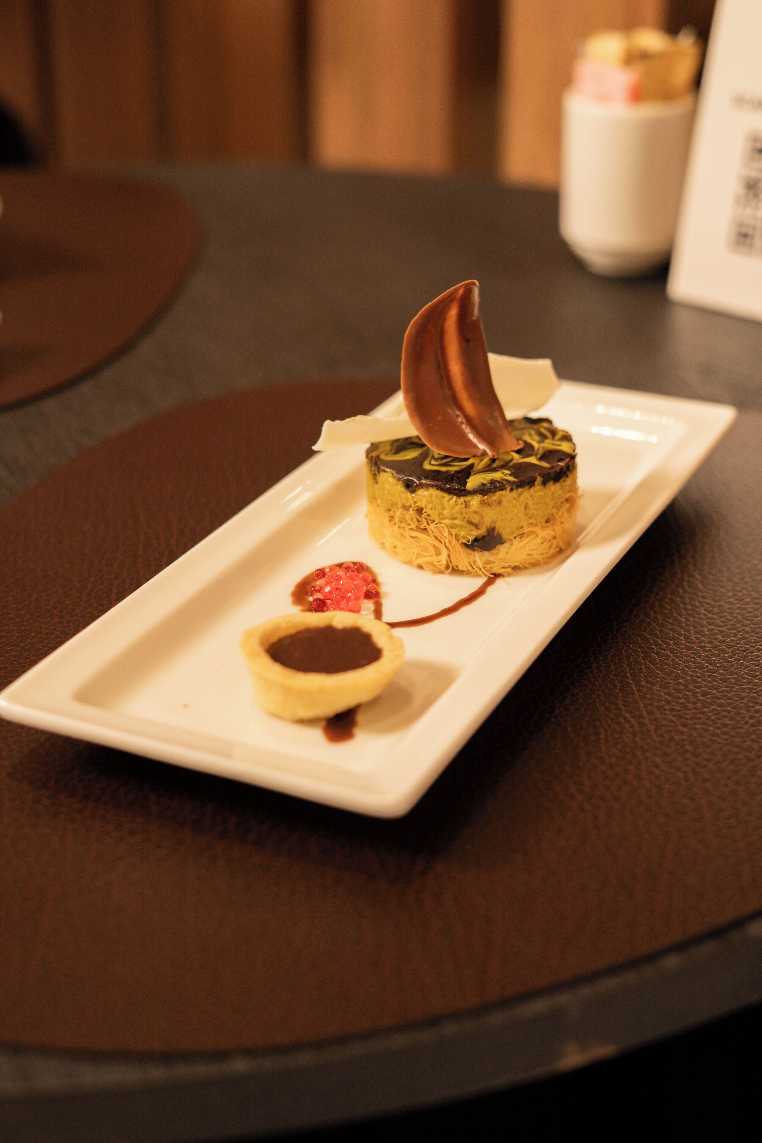 A dessert on a white rectangular plate with a chocolate piece on top, placed on a dark table.