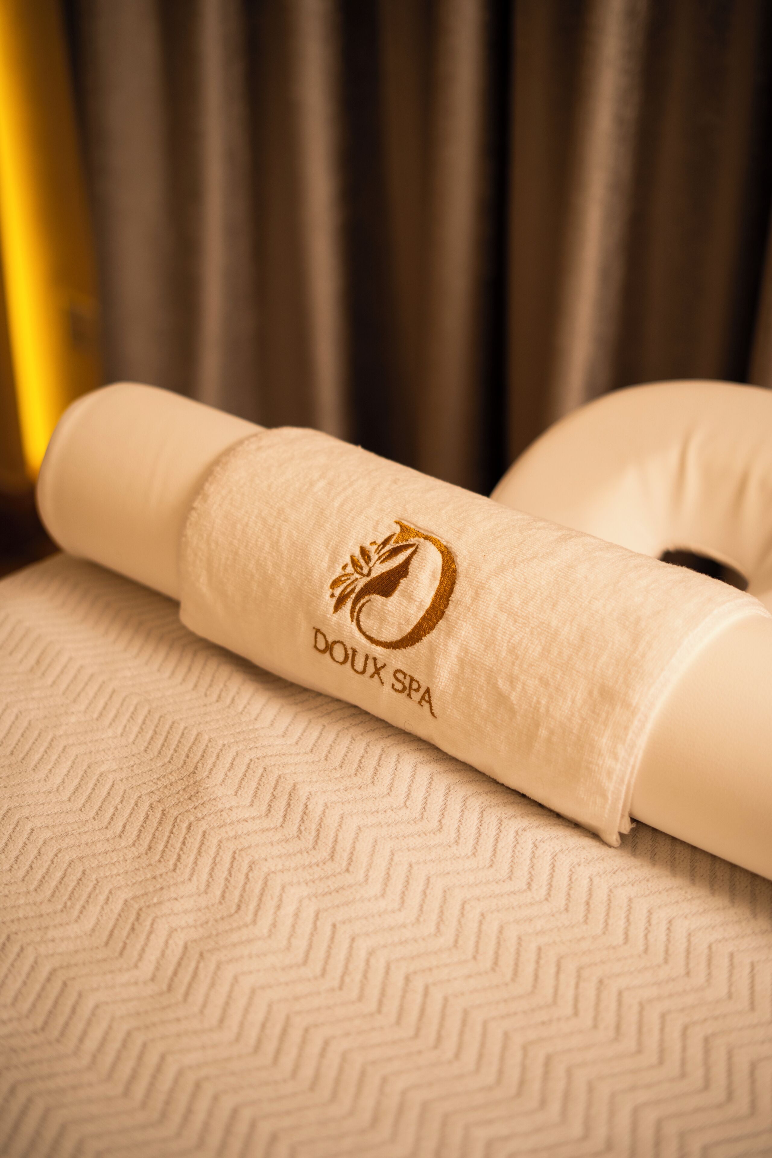 A rolled towel with 'Doux Spa' embroidered on it, placed on a textured surface.