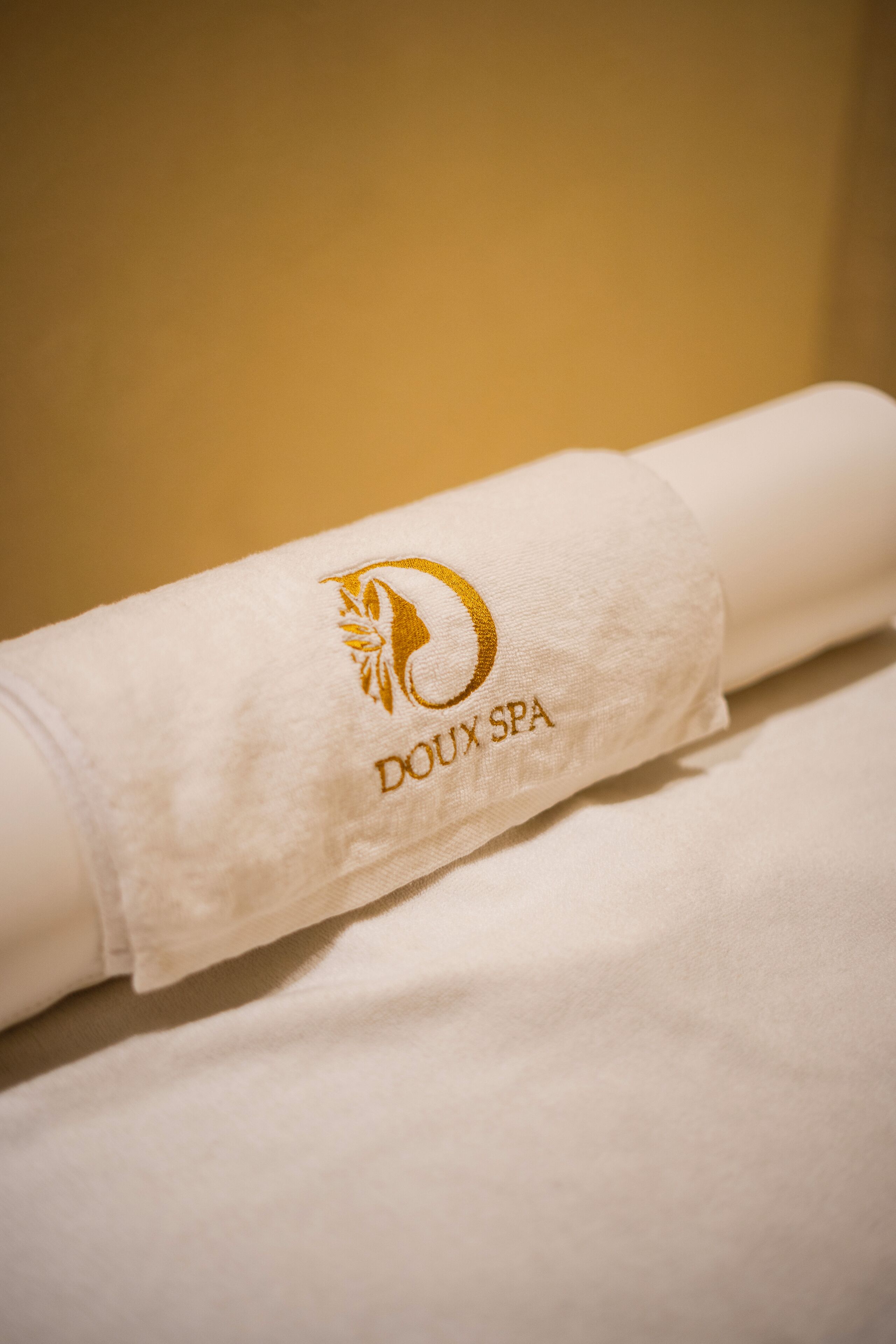 A rolled towel with embroidered text 'Doux SPA' and a golden emblem.