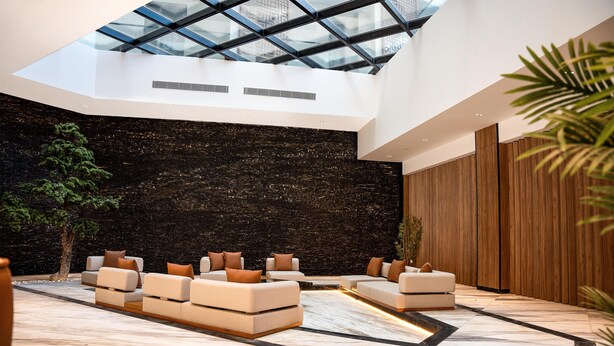 A modern interior with a high ceiling, a black textured wall, and a seating area with sofas and a coffee table. - Golden Tulip Muscat The Village (Seeb)