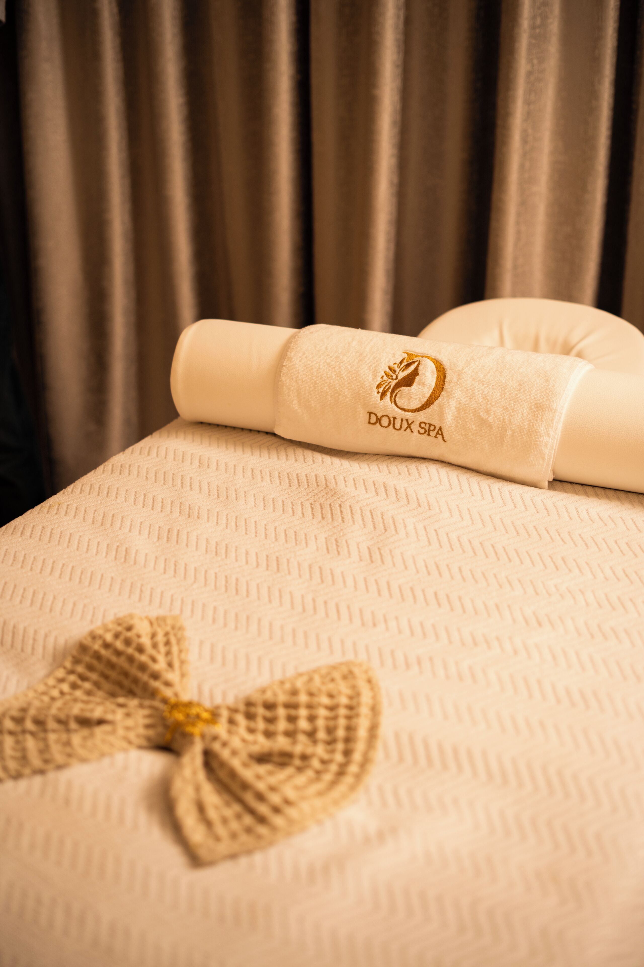 Una camilla de spa con una toalla y un lazo decorativo, y un logo que dice 'DOUX SPA'.