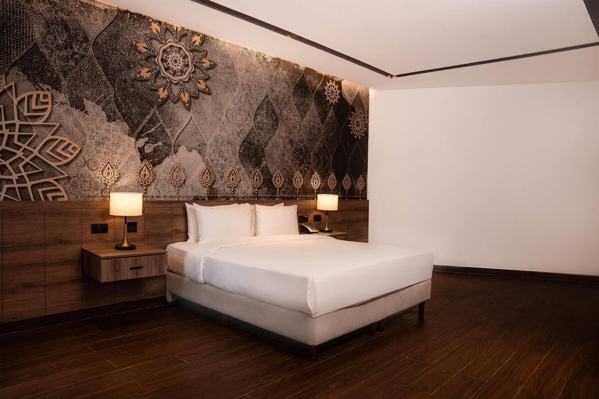 Una camera d'hotel moderna con un letto grande, due comodini e un murale decorativo.