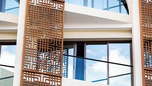 A modern building with multiple floors, large windows, and decorative wooden lattice panels. - Golden Tulip Muscat The Village (Seeb)