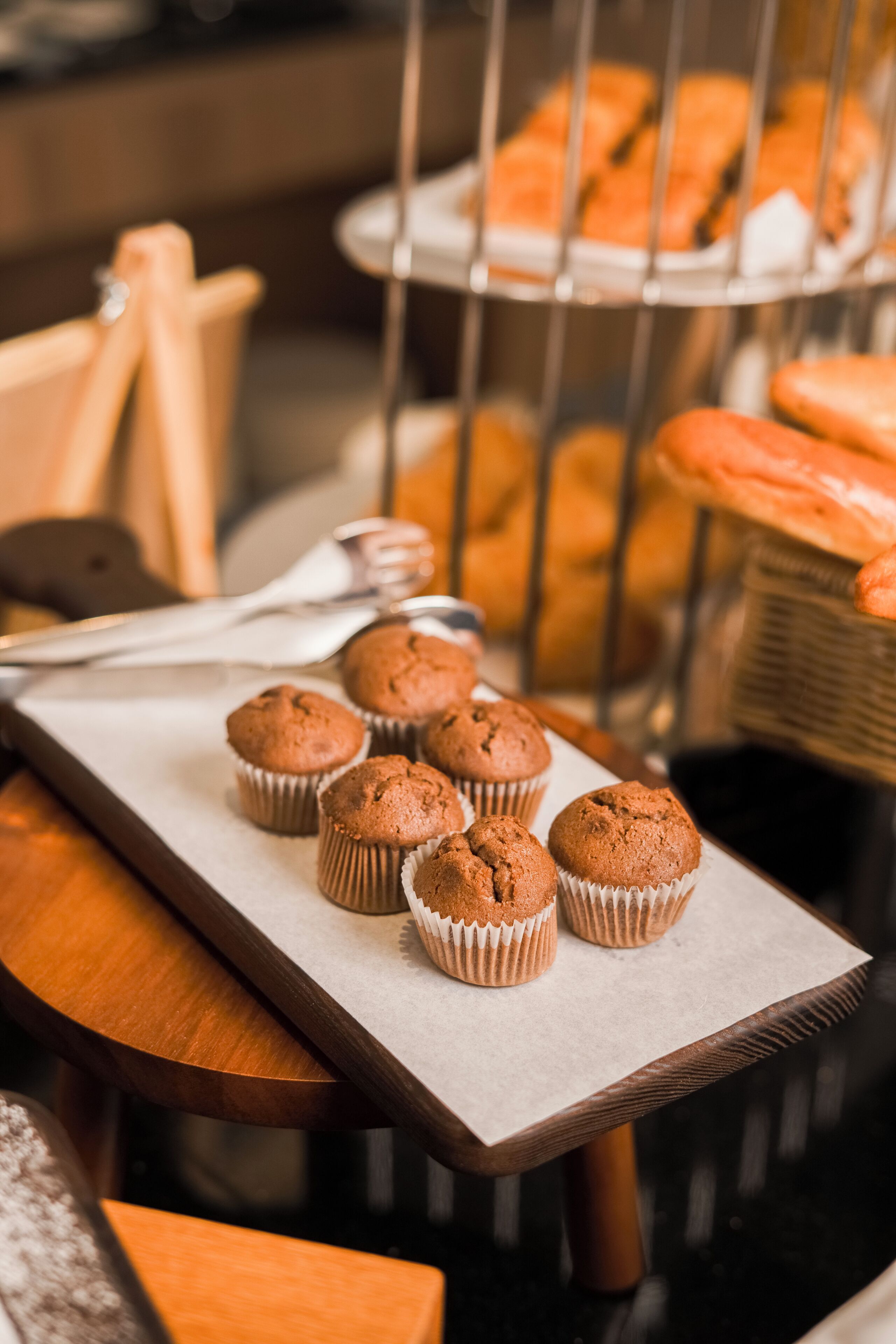 Una bandeja de muffins sobre una mesa de madera, con un estante metálico al fondo.