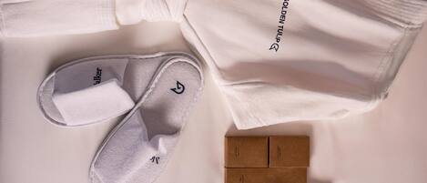 A neatly arranged set of white slippers, a white robe, and three brown boxes on a white surface.