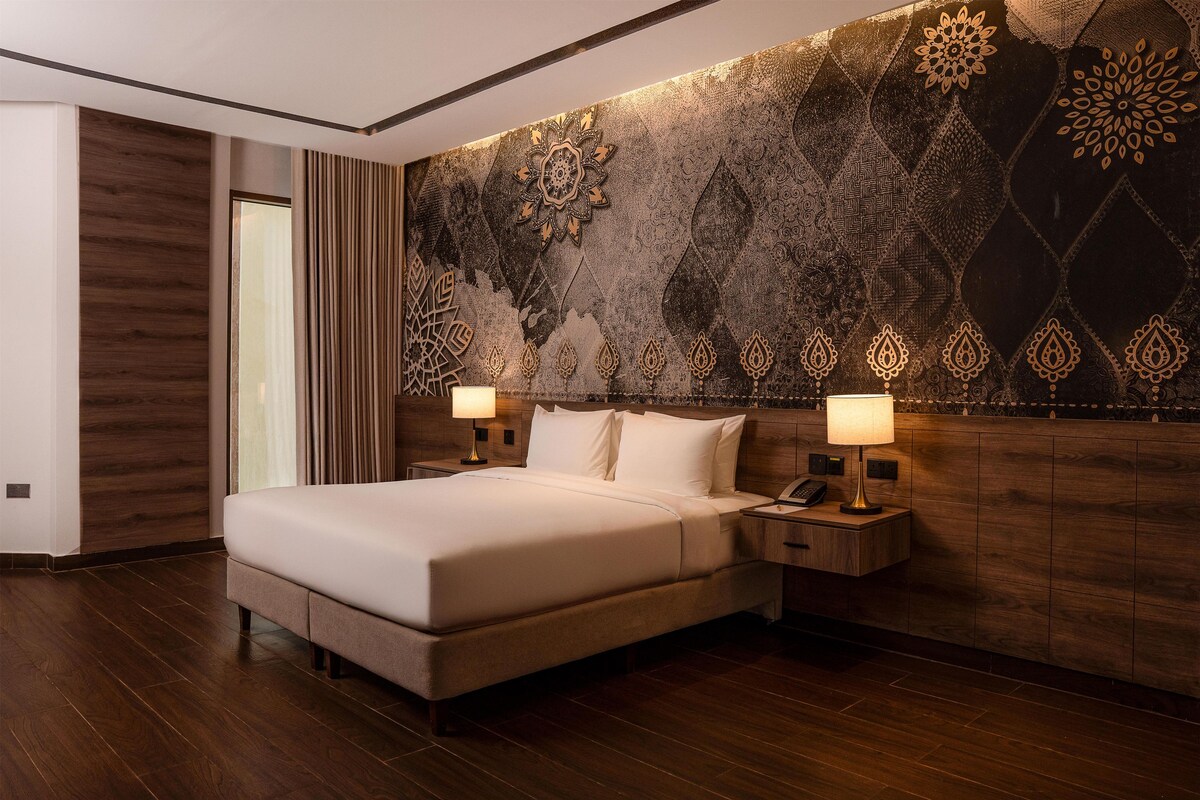 Ein modernes Hotelzimmer mit einem großen Bett, einem Holz-Kopfteil und dekorativen Wandmustern.