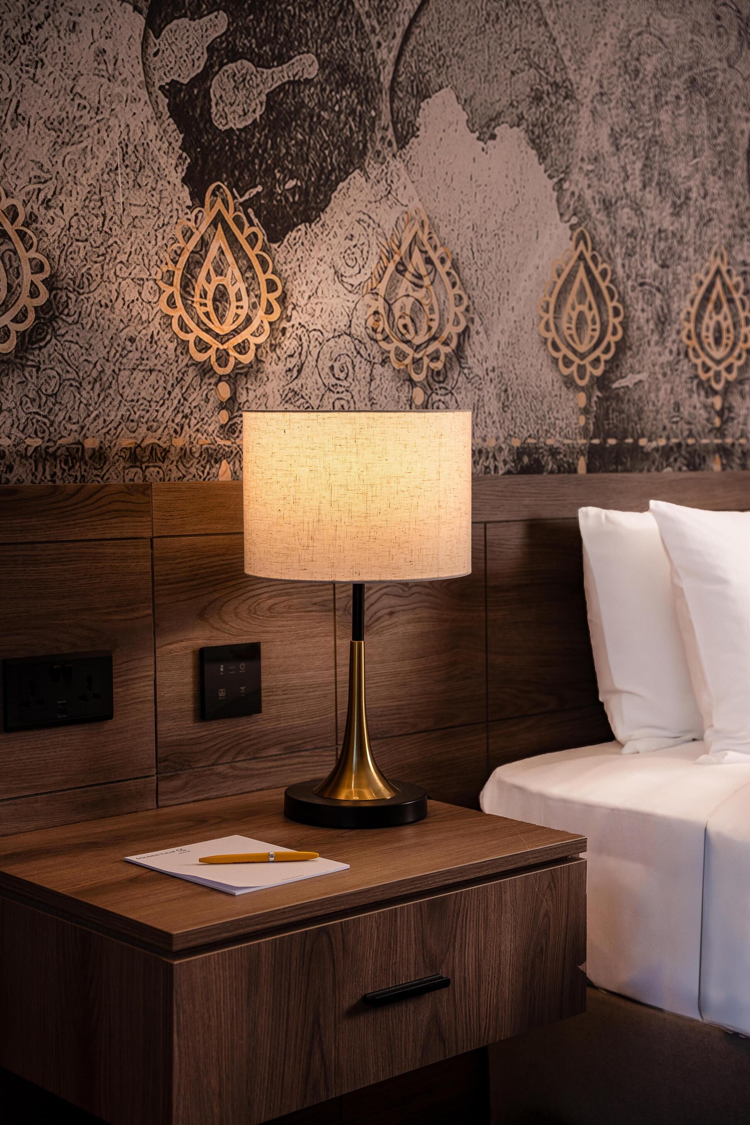 A wooden nightstand with a lamp, a notebook, and a pen.