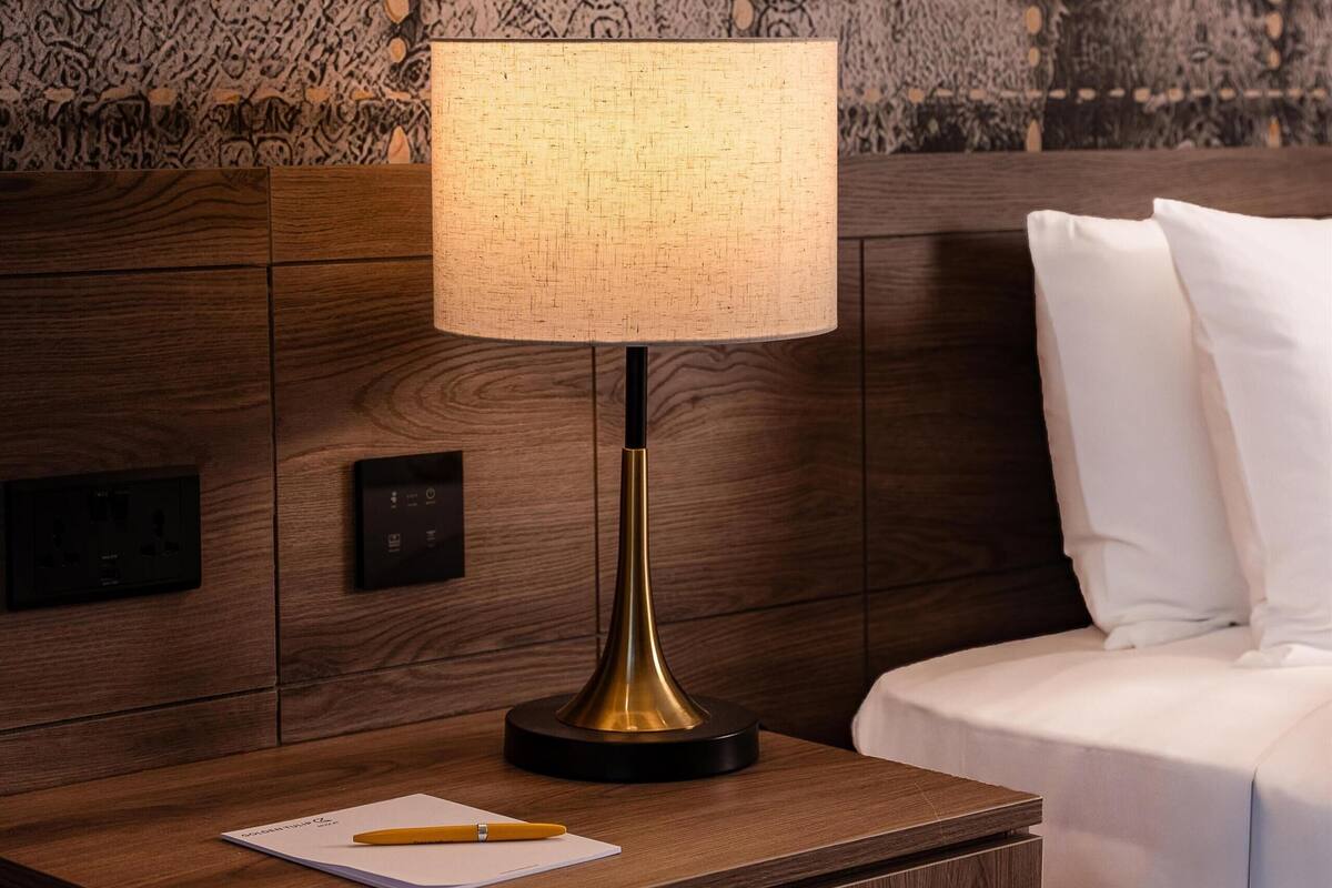 Un comodino in legno con una lampada, un quaderno e una penna.
