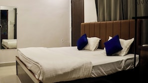 Un lit bien fait, avec du linge de lit blanc et deux oreillers bleus, une tête de lit en bois, une porte marron foncé et un miroir au mur.
