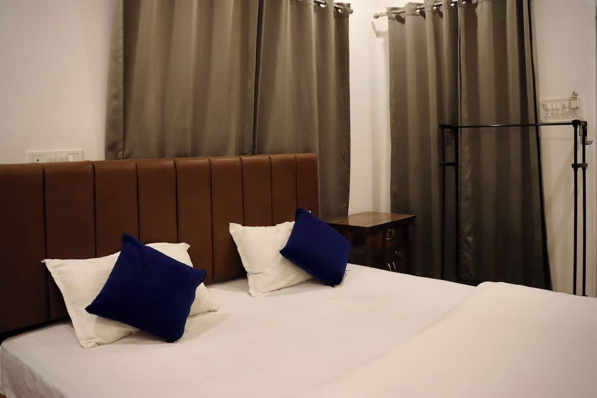 A hotel room with a bed, brown headboard, white and blue pillows, a wooden nightstand, and a black floor lamp.