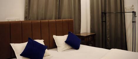 A hotel room with a bed, brown headboard, white and blue pillows, a wooden nightstand, and a black floor lamp.