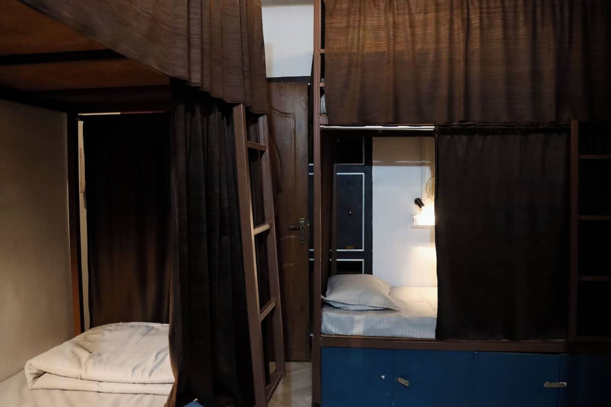 A small, compact room with a bunk bed and a single bed. There is a wooden door and a window with curtains.