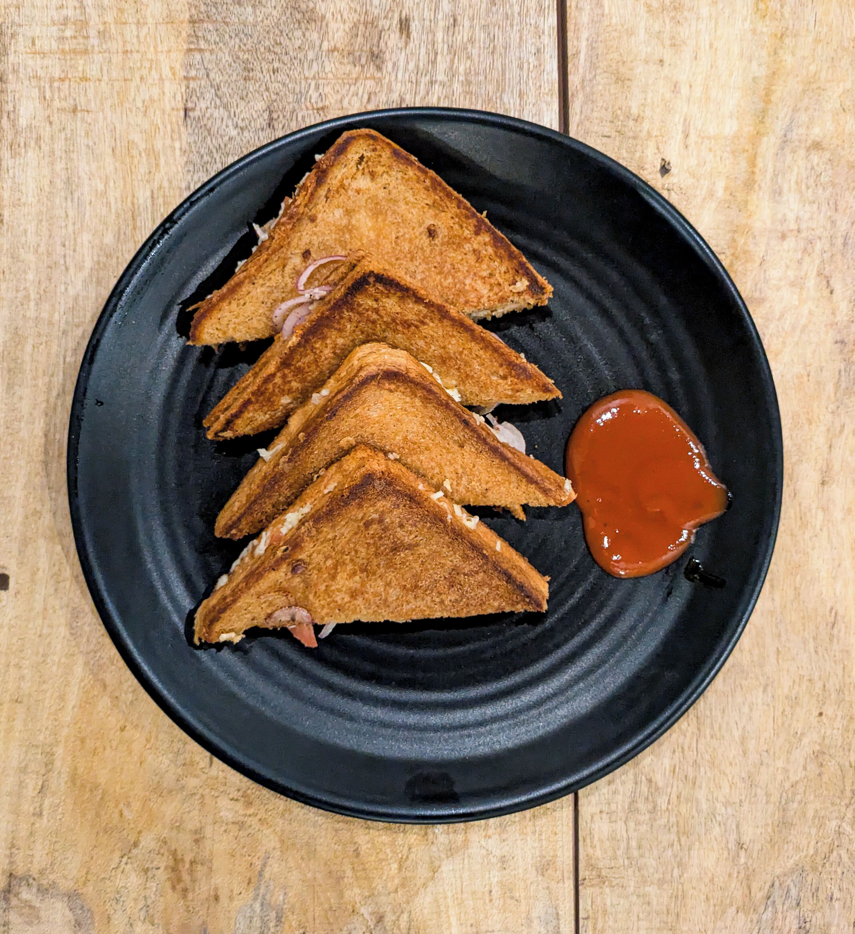 Four grilled sandwiches on a black plate with a side of sauce.