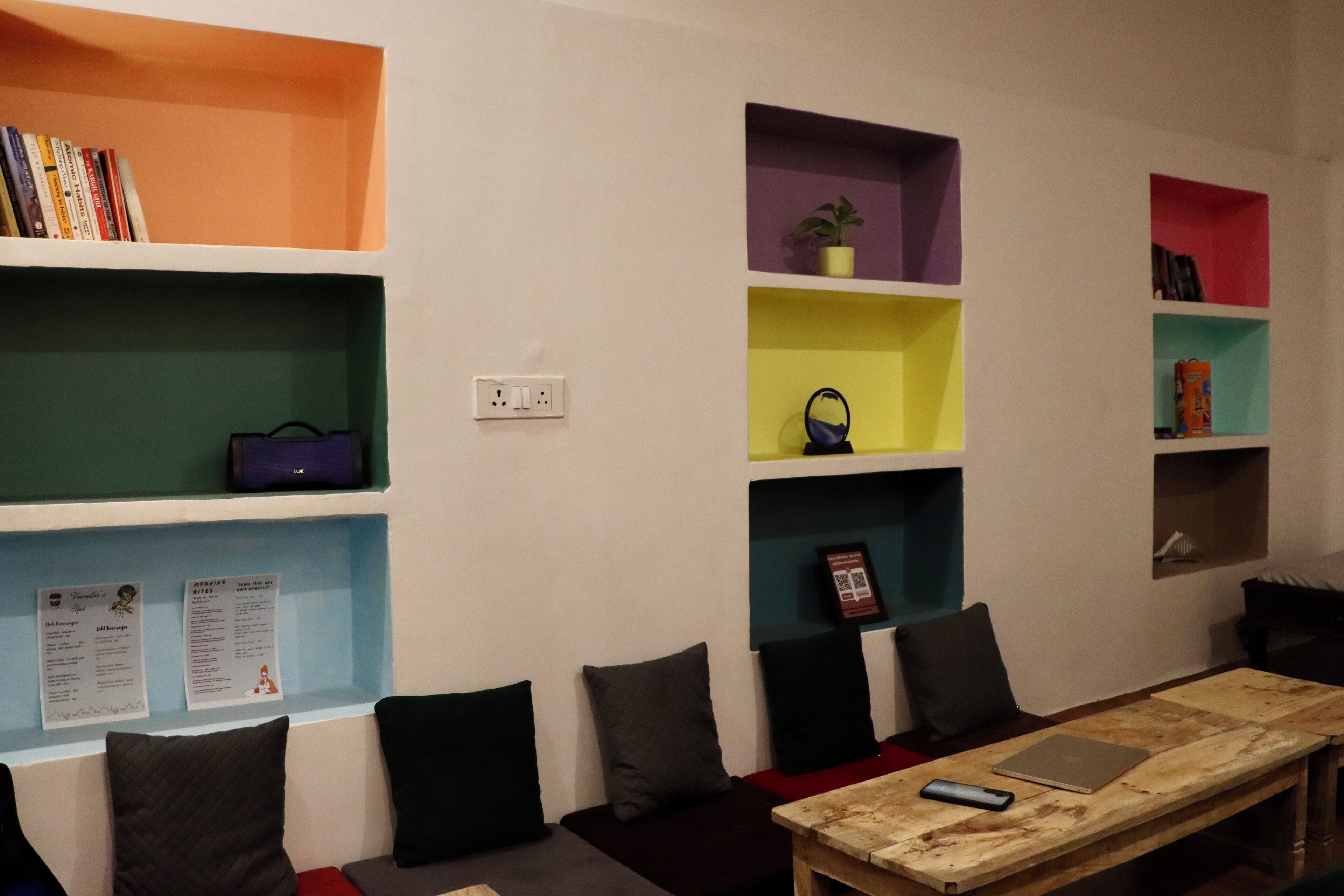 A room with a wooden table, multiple shelves with books and decorative items, and a seating area with cushions.