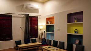 Un salon chaleureux avec une table en bois, des bancs et une guitare. On y trouve des étagères remplies de livres et une plante en pot.