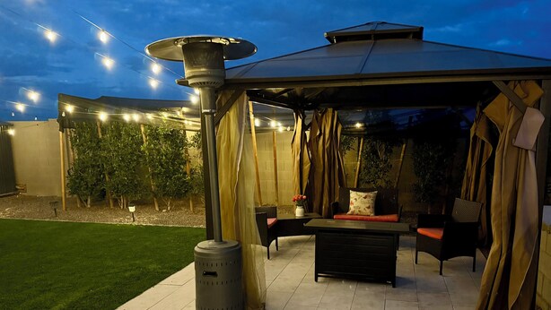 Een terras buiten met een overdekte zithoek, een heater en lichtslingers.