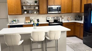 Een moderne keuken met houten kastjes, een roestvrijstalen magnetron, een zwarte koelkast en een wit kookeiland met barkrukken.