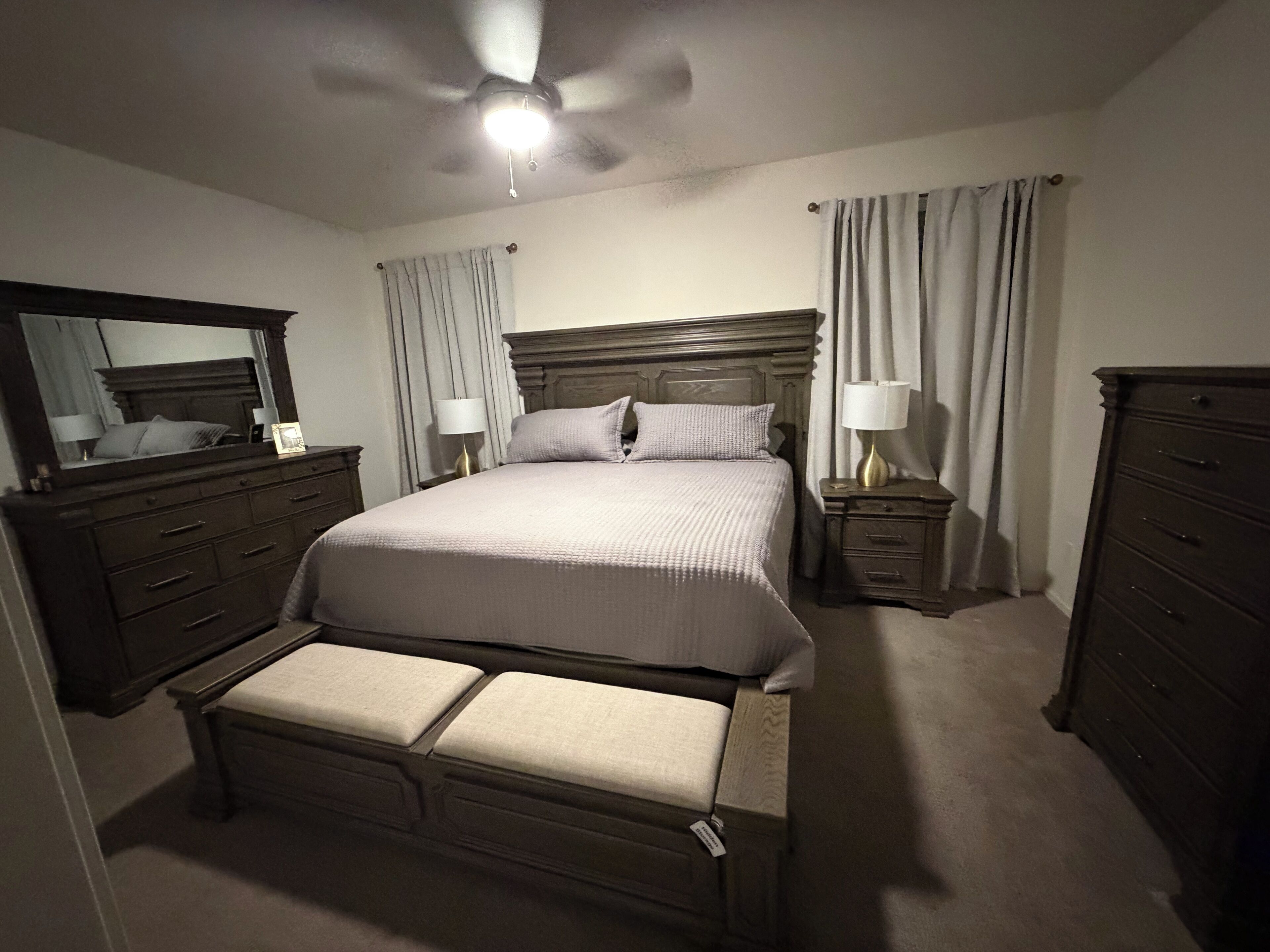 Une chambre à coucher comprenant un lit, des tables de chevet, une commode, un miroir et un ventilateur de plafond.