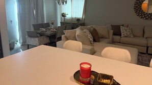 Een woonkamer met een eethoek, een zithoek, een kroonluchter en een decoratieve spiegel.