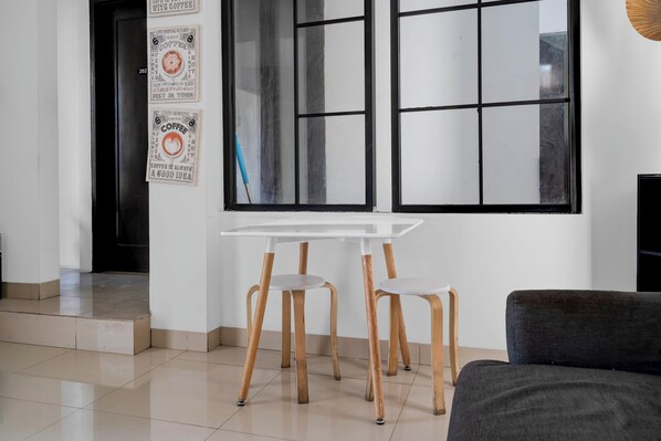 A modern room with a white table and two wooden chairs, a dark sofa, and a large window with a view.