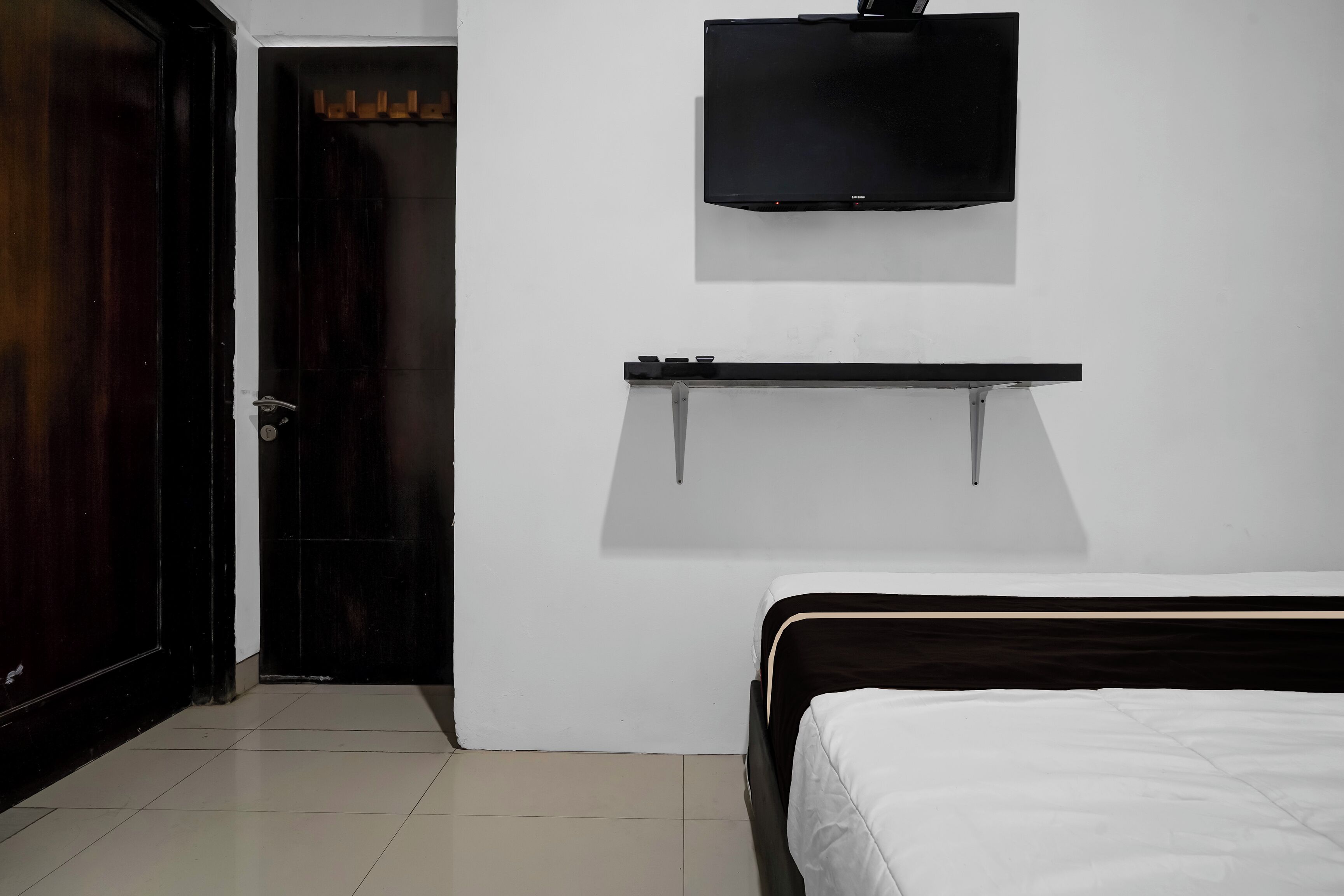 A bedroom with a bed, a TV mounted on the wall, and a door leading to another room.