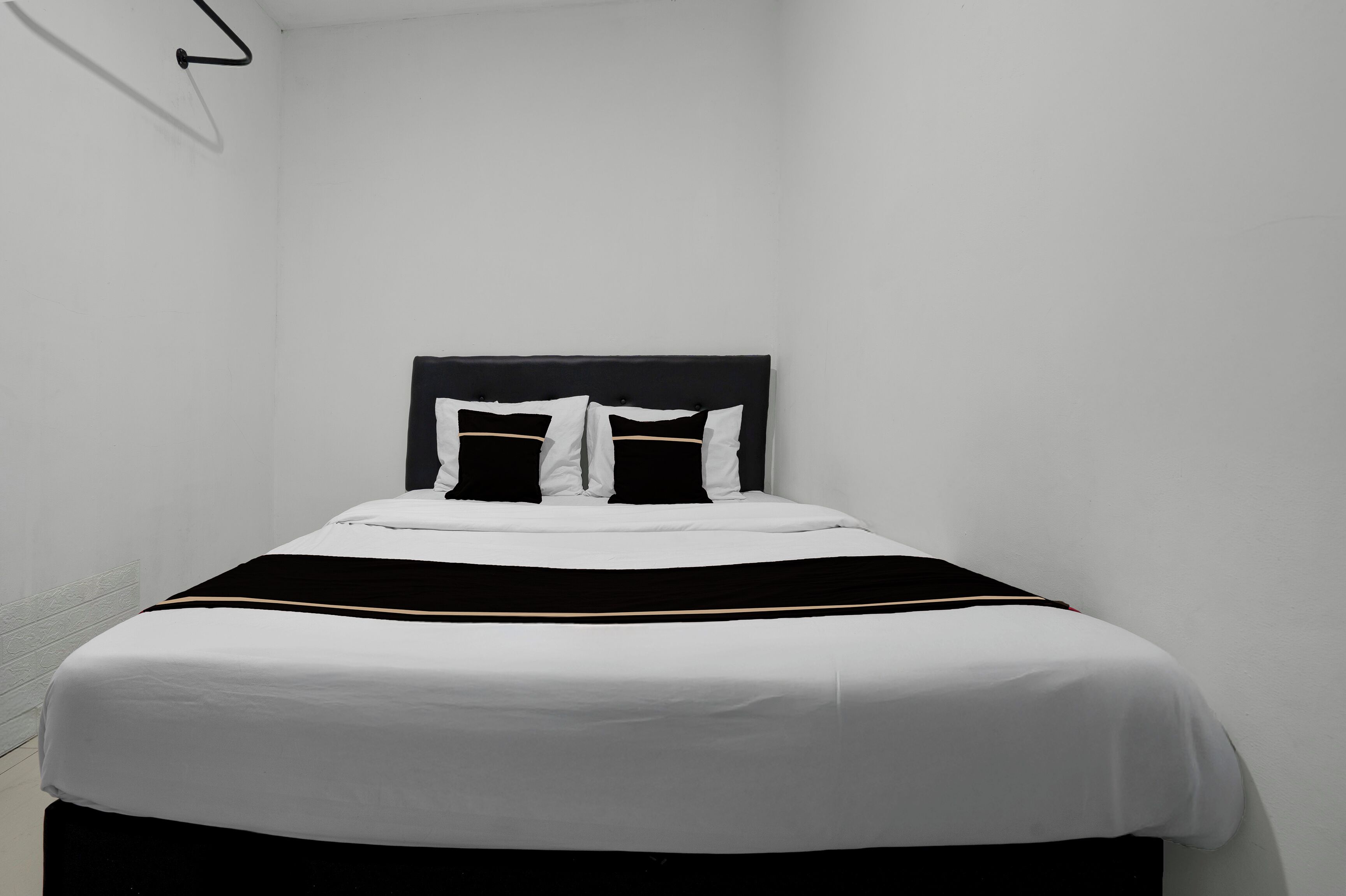 A single bed with a black headboard and white bedding in a room with white walls.