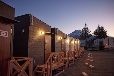 A row of wooden portable toilets with illuminated signs, a mountain in the background, and a clear sky.