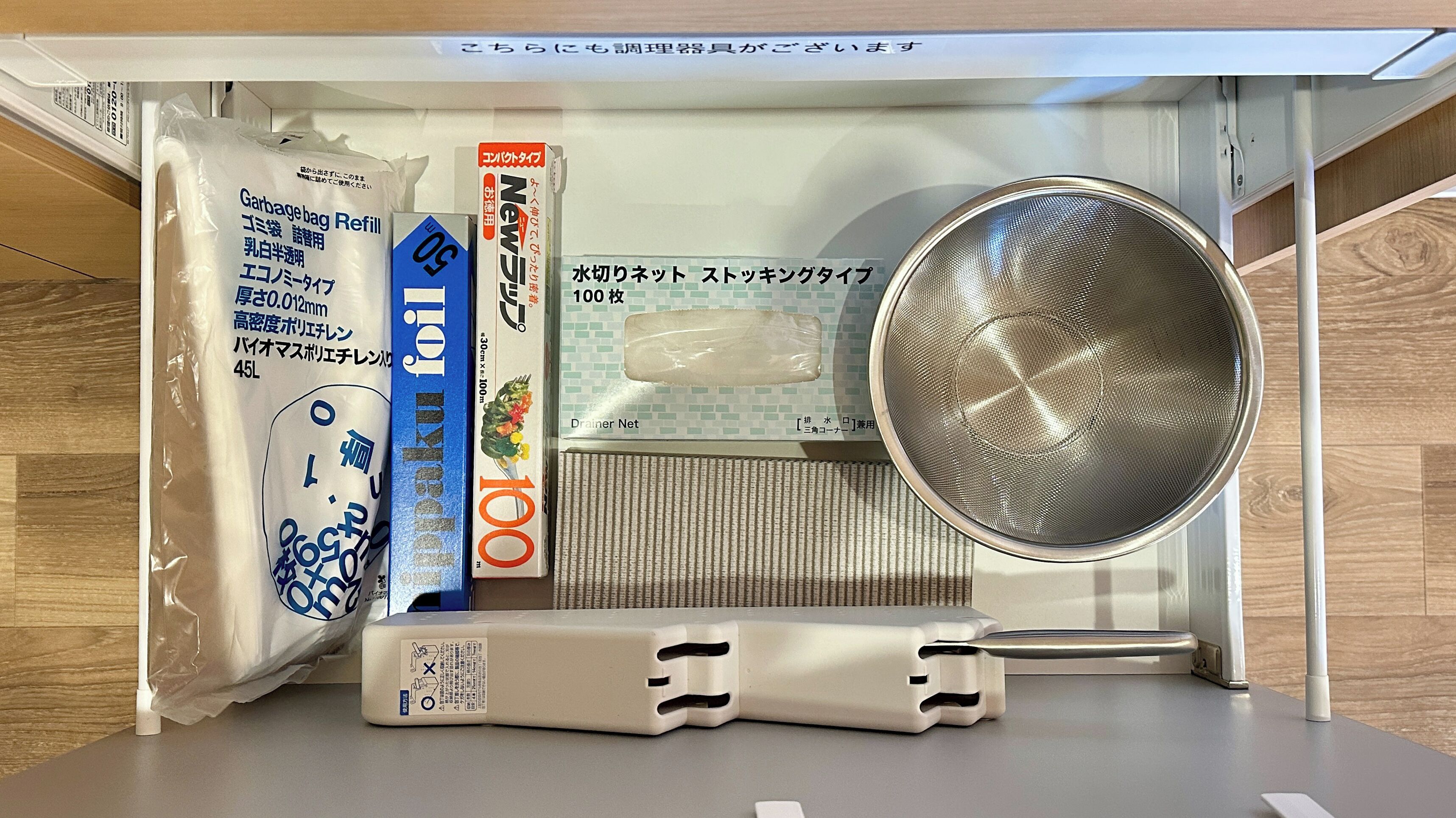 Un coin cuisine comprenant un rouleau de sacs à ordures, une bouteille bleue, une boîte blanche et une passoire en métal.